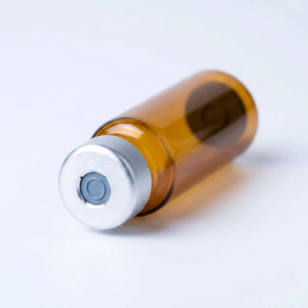 Macro of the amber cartridge's silver crimped aluminum cap: punched-open center exposing the rubber septum disc over amber borosilicate glass