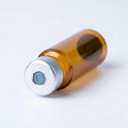 Macro of the amber cartridge's silver crimped aluminum cap: punched-open center exposing the rubber septum disc over amber borosilicate glass