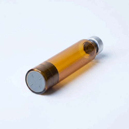 Amber 3 ml glass pen cartridge lying at a diagonal: flat gray rubber plunger face flush in the open amber glass end, silver crimped cap at the far end