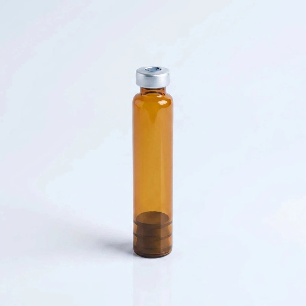 Amber borosilicate 3 ml glass pen cartridge standing upright: silver crimp cap with center septum on top, rubber plunger seated inside the amber glass at the base