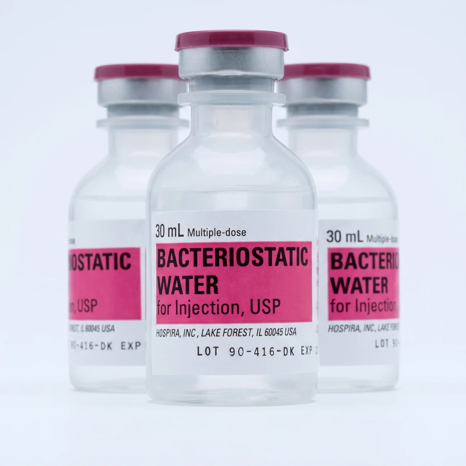 Three 30 ml Pfizer Hospira bacteriostatic water vials arranged on a pale studio backdrop