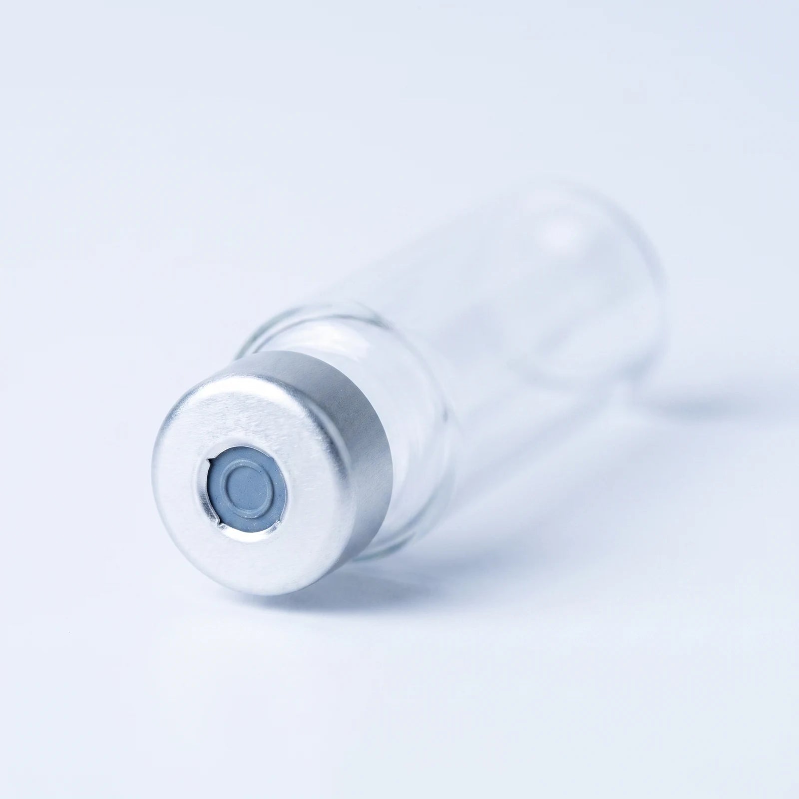 Macro of the cartridge's silver crimped aluminum cap: punched-open center exposing the blue-gray rubber septum disc