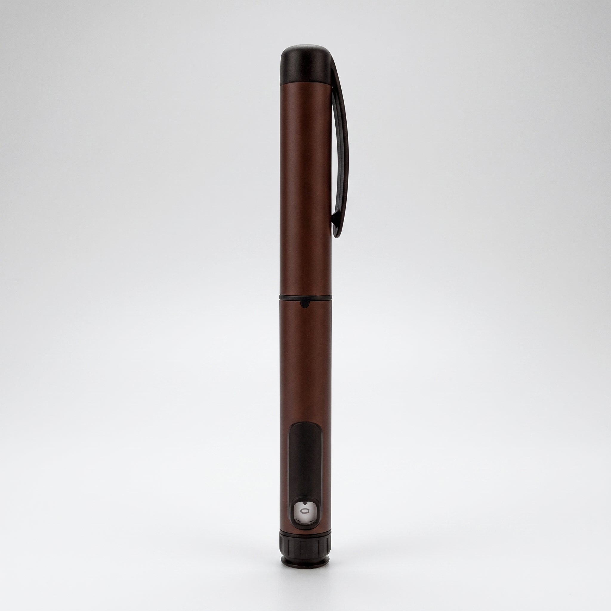 Dark brown V1 Peptide Pen, reusable manual click-dial pen, standing upright on a pale studio background