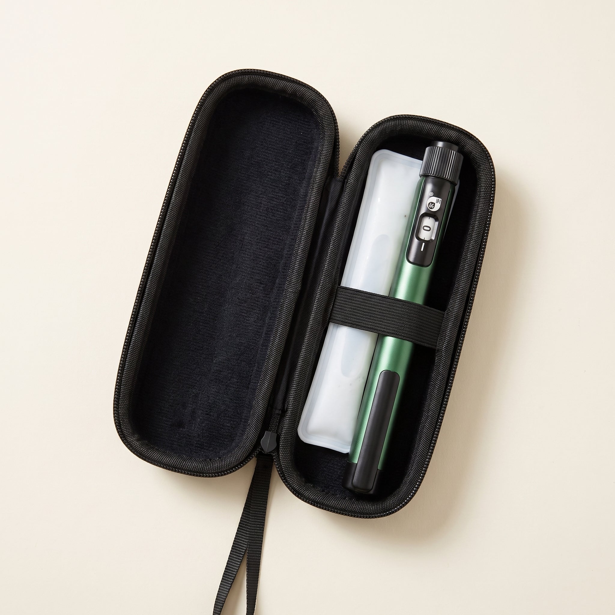 Open black EVA travel case holding a green pen and a white ice pack under an elastic strap