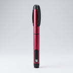 Crimson red V1 Peptide Pen, reusable manual click-dial pen, angled diagonally on a pale studio background